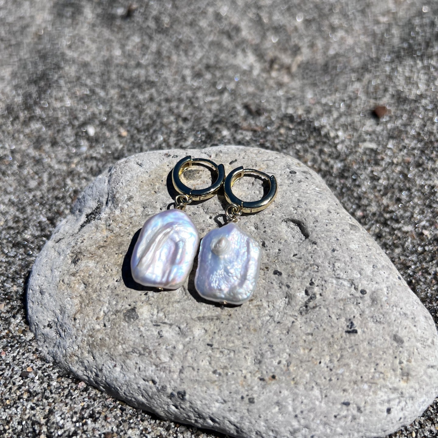 Pearl earrings on a stone with a beach background