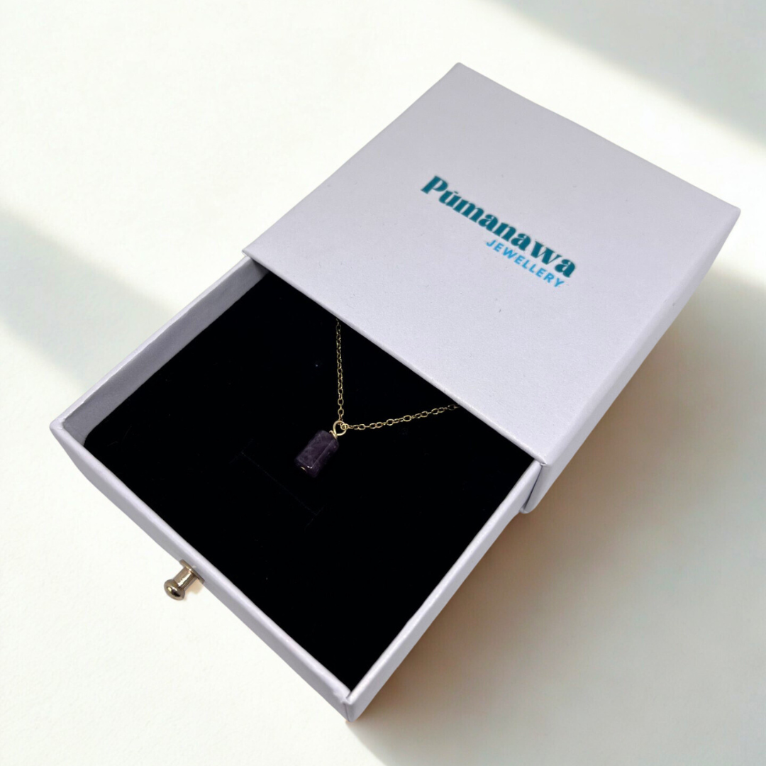Necklace with a purple pendant in an open white box with 'Pumanawa Jewellery' branding.
