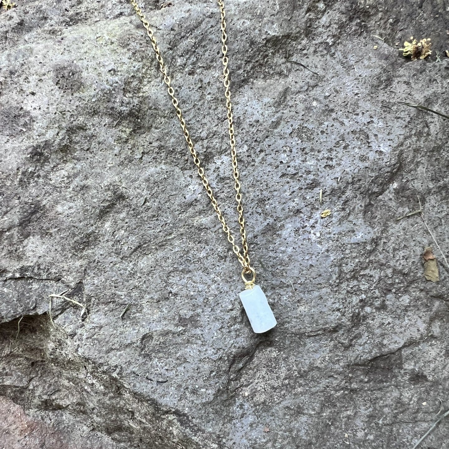 Gold necklace with a small pendant on a stone surface