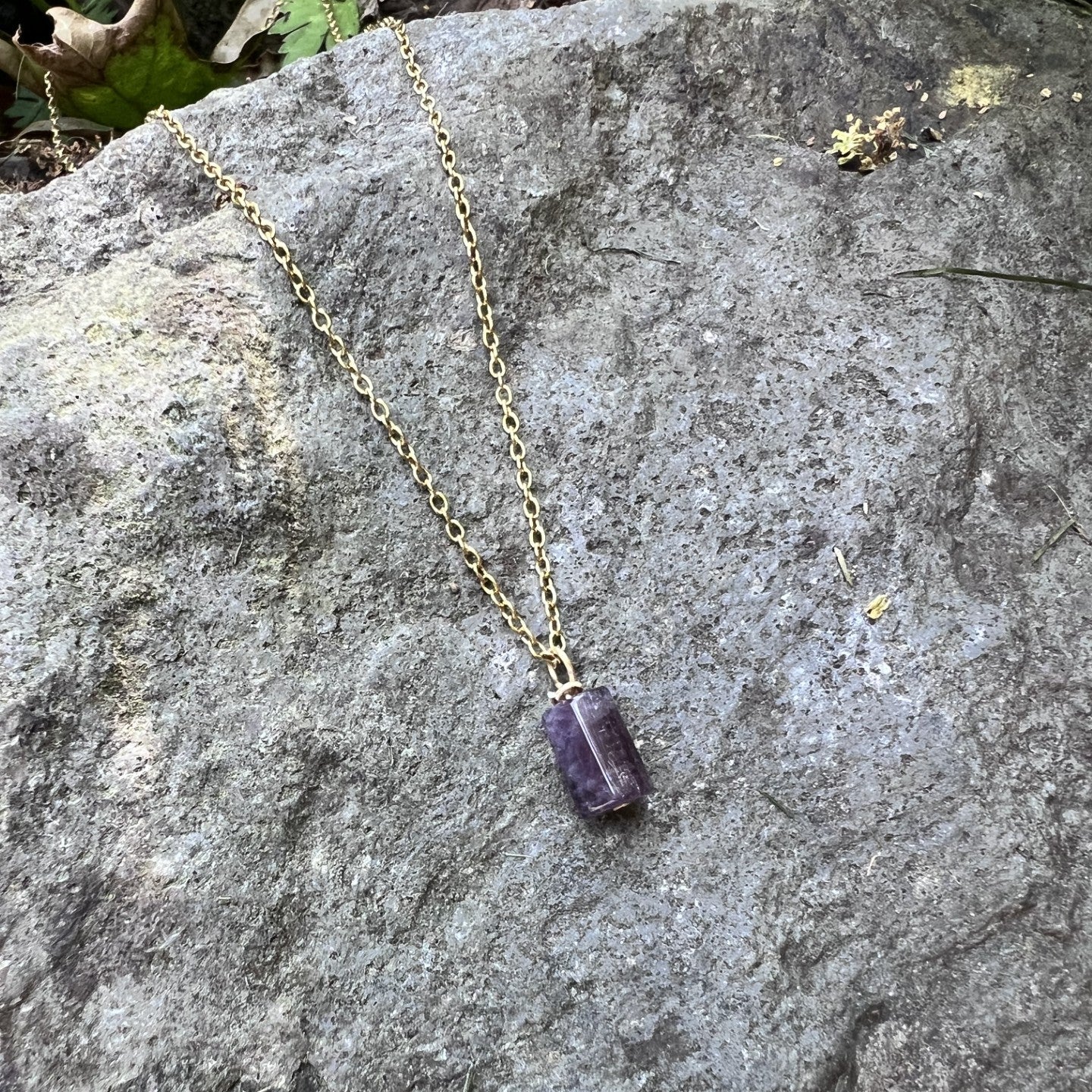 Necklace with a purple pendant on a rock