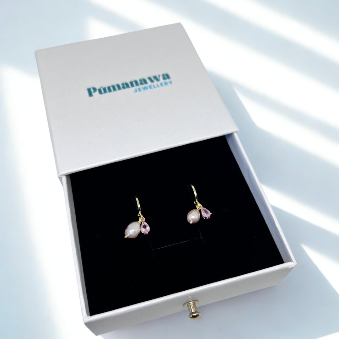 Pair of earrings in a Pumanawa Jewelry box on a light blue background