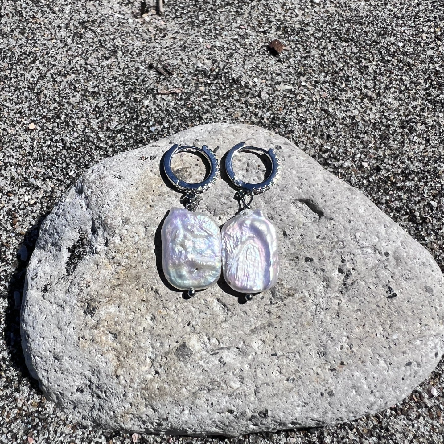 Pair of pearl earrings on a stone with a sandy background