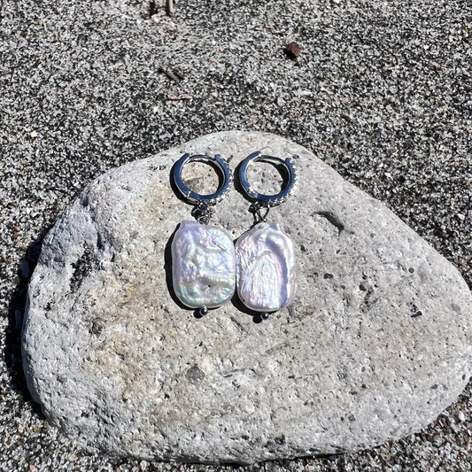 Pair of pearl earrings on a stone with a sandy background