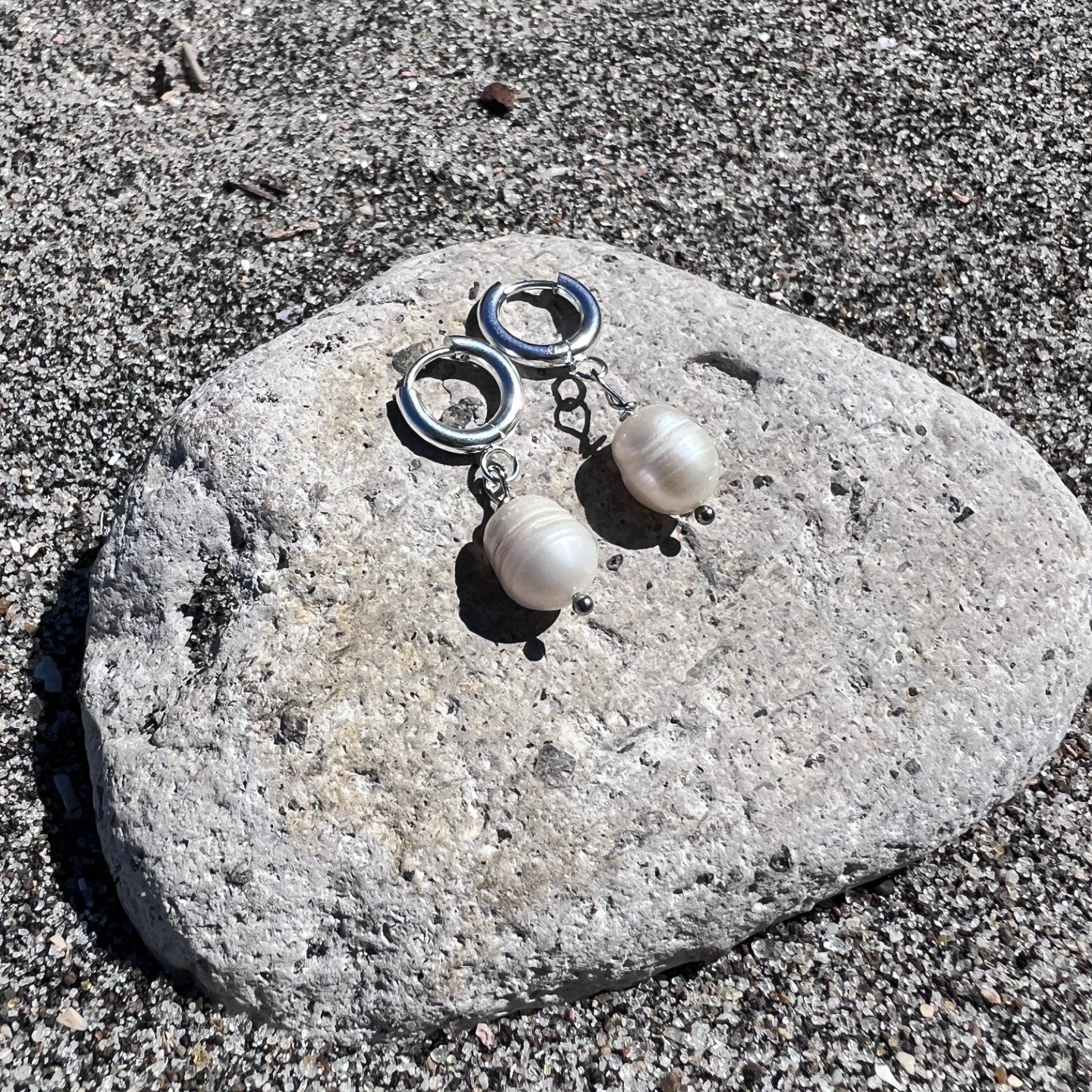 Pair of silver earrings with round stones on a stone surface