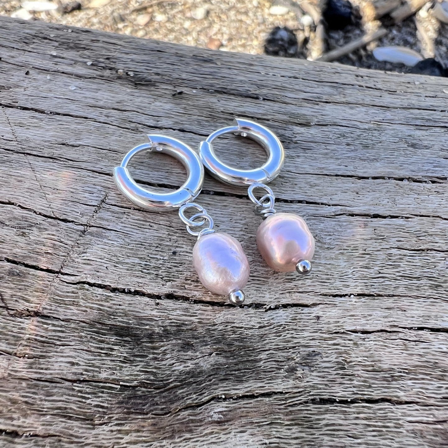 Silver hoop earrings with pink pearls on a wooden surface